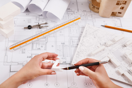 Architect making architectural project. Top view on unrecognizable designer hands working with plastic details on building blueprint, copy spaceの写真素材