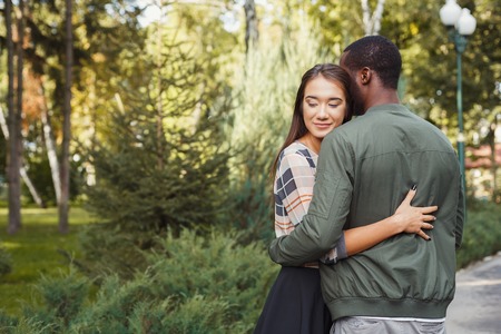 Portrait of happy multiracial couple hugging in park in sunny day, copy space. Love story, romantic dateの写真素材