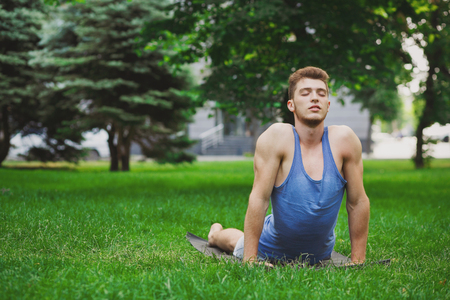 Fitness, young man training yoga in cobra pose in park. Sporty guy with closed eyes makes exercise outdoors, copy spaceの写真素材