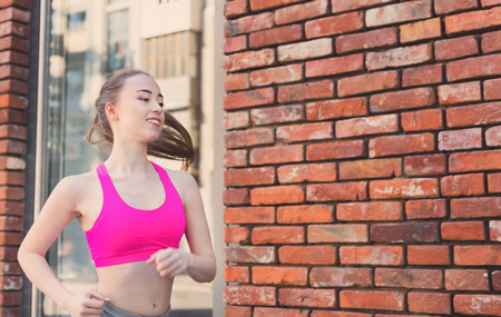Young blonde woman running in city near brick building with mirror windows, copy spaceの写真素材