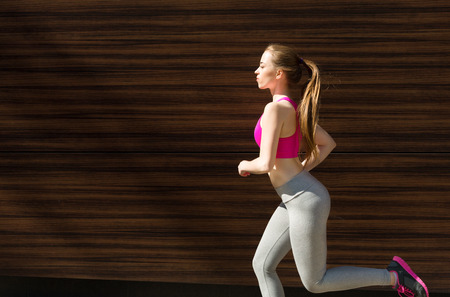 Young blonde woman running in city near wooden wall, copy spaceの写真素材