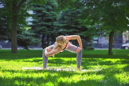 Fitness, woman training yoga pose outdoors in the park, copy space. Young slim girl makes exercise. Stretching, wellness, calmness, relax, healthy, active lifestyle conceptの写真素材