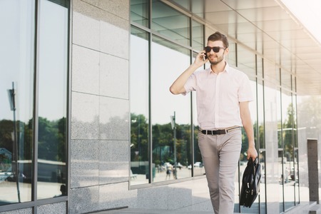 Confident successful businessman talking on smartphone outdoors. Young stylish executive having important conversation at modern building, copy spaceの写真素材
