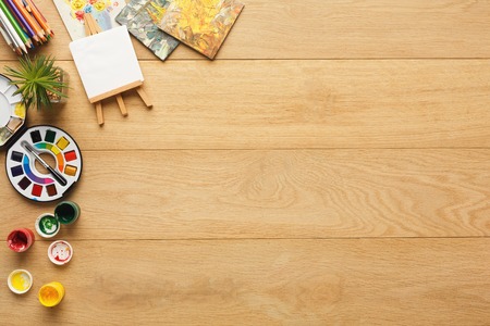 Border of various stationery for art, top view. Light wooden desktop with pencils, colors, paper. Studying and creative background, copy spaceの写真素材