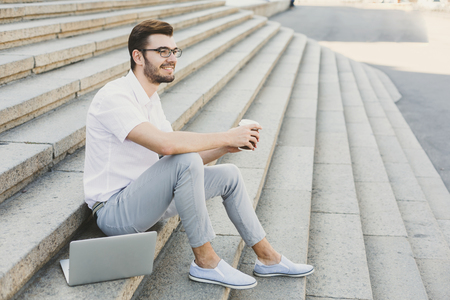 Pensive businessman having rest outdoors. Young serene salesman sitting on stairs with take away coffee, copy spaceの写真素材