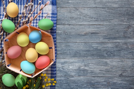 Easter background with copy space. Colorful eggs, holiday decoration in basket on rustic table top...
