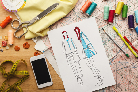 Creating new fashion collection background. Hand drawn sketches of clothes, smartphone, color swatches and threads on wooden table, top view. Creativity, dressmaking and design conceptの写真素材