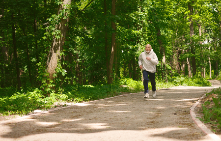 Elderly sporty man running in green forest during morning workout, copy space. Healthy and active lifestyle at any age conceptの写真素材