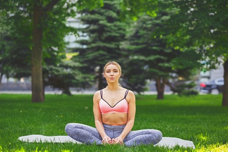 Young woman outdoors, butterfly pose. Girl does lotus pose for relaxation. Wellness, calmness, relax, healthy, active lifestyle conceptの写真素材