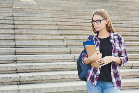 Serious student girl with books on university stairs background, looking away, dreaming or thinking during break, having rest in campus. Education concept, copy spaceの写真素材