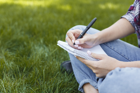 Female hands with notebook closeup, over shoulder shot. Woman studying outdoors with note-book. Education, inspiration and remote working concept.の写真素材