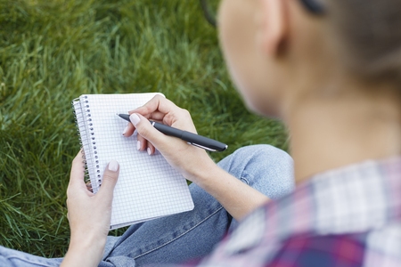 Female hands with notebook closeup, over shoulder shot. Woman studying outdoors with note-book. Education, inspiration and remote working concept.の写真素材