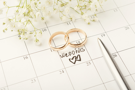 Word wedding, two hearts and gold rings on calendar with sweet white flowers. Love, invitation, advertisement, romantic background concept, copy spaceの写真素材