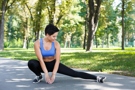 Fitness woman stretching her legs before running outdoors. Young slim girl makes aerobics exercise in park, copy spaceの写真素材