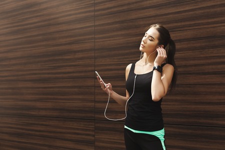 Woman choose music to listen in her mobile phone during workout in city, having rest at wooden wall, copy spaceの写真素材