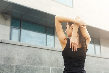 Fitness woman stretching her back before running outdoors, back view. Young slim girl makes aerobics exercise, gray wall background, copy spaceの写真素材