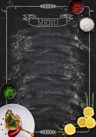 Design concept for restaurant menu mockup. Black rustic chalkboard with white inscription and vegetables frame, top view, copy space for text and logoの写真素材