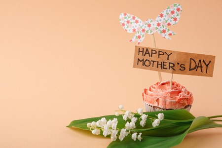 Mothers day background, handmade greeting card in tasty cupcake and may-lily at tender beigebackdrop. Present for mommy, copy spaceの写真素材