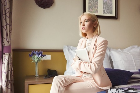 Portrait of serious businesswoman sitting on bed and holding digital tablet. Woman working in hotel room. Business lady went to business trip and stayed at the hotel, copy spaceの写真素材