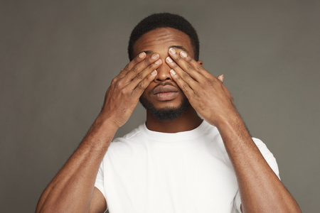 Black man covering eyes with hands on grey studio background, copy spaceの写真素材
