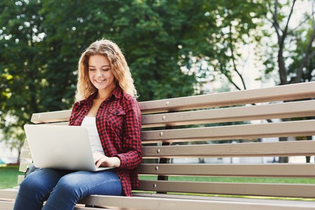 Smiling casual woman, freelancer working with laptop in the park in pleasant atmosphere. Technology, communication, education and remote working concept, copy spaceの写真素材
