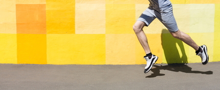 Unrecognizable athlete man running against bright yellow graffiti wall, copy space, cropの写真素材
