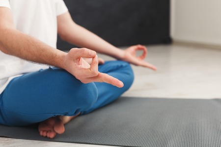 Closeup of unrecognizable man hands, meditating, sitting in lotus pose on mat, copy spaceの写真素材
