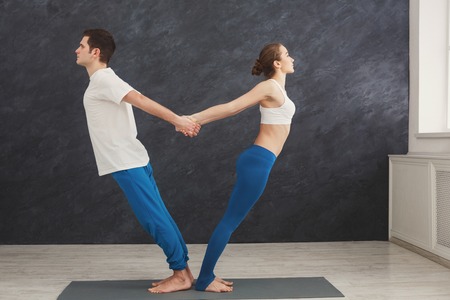 Man and woman training yoga in balance pose. Young couple making relaxing exercise, standing back to back, copy space. Partner yoga conceptの写真素材