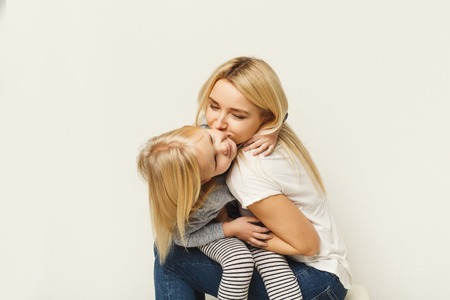 Happy casual mother and little daughter embracing and kissing at white studio background. Portrait of cute smiling girls. Family, mother love and mother`s day concept, copy spaceの写真素材