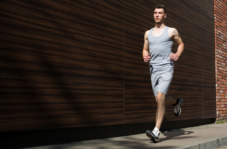 Young man running in city, dark wooden wall background, copy spaceの写真素材