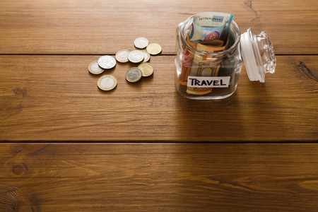 Travel budget concept. Money saved for vacation in glass jar on wooden background, copy space, top view. Banknotes and coins for big adventure.の写真素材