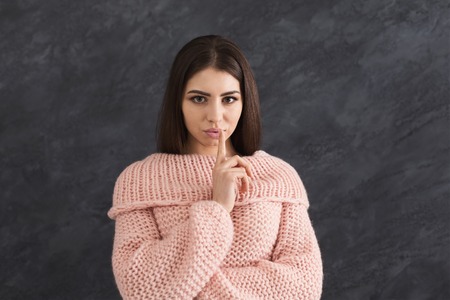 Secret. Young woman put finger on lips, hush sign, keep silence. Girl on dark backgroundの写真素材