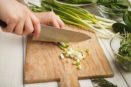 Woman cutting spring onion on wooden board for salad. Preparing organic food, natural homemade eating, copy spaceの写真素材