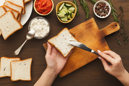 Woman cooking tasty sandwich with cream cheese, top view. Female hands spreading bruschetta topping on bread. Healthy eating conceptの写真素材