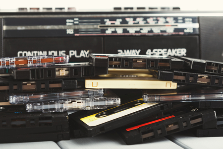 Heap of retro audio cassettes and vintage tape recorder on gray background. Side view on old-fashioned media devices, copy space, flat layの写真素材