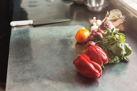 Cooking healthy meals at professional kitchen. Organic vegetables, wooden cutting board, sharp chef knife on steel tableの写真素材