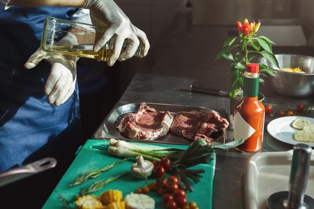 Unrecognizable male chef preparing vegetables for salad, marinating fresh beef steaks at professional hotel or restaurant kitchenの写真素材