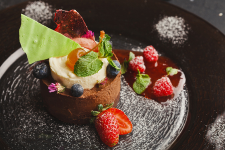 Exquisite restaurant mousse dessert. Chocolate and vanilla souffle on walnut biscuit served on glass plate finely decorated with fresh berries and mint. Exclusive meals and haute cuisine conceptの写真素材