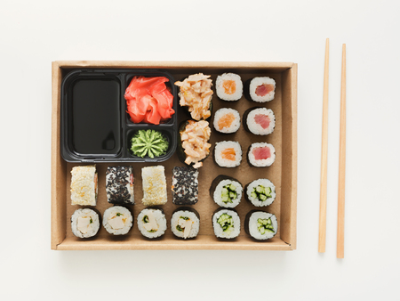 Japanese restaurant, sushi rolls in wooden platter isolated on white background. Set for one person, with chopsticks, ginger, soy sauce and wasabi. Top view, copy spaceの写真素材