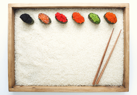 Top view on sushi gunkan with colored caviar in wooden frame with chopsticks on white rice background and texture copy spaceの写真素材