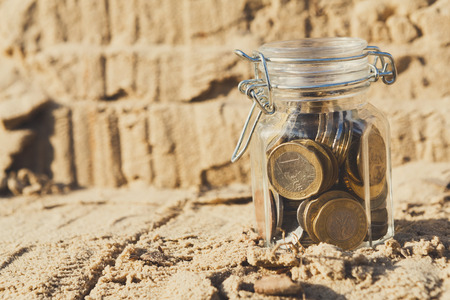 Coins in glass jar on rock background, copy space. Money box, saving money for dream, pension, vacation. Financial stability conceptの写真素材