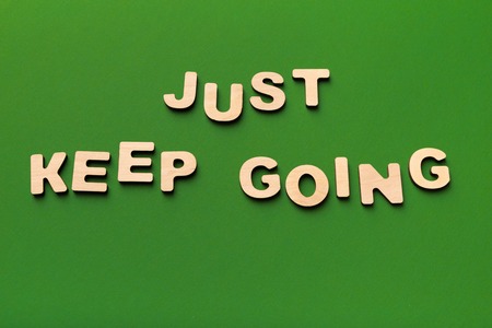 Motivation poster. Phrase Just keep going spelled with wooden letters on green background....