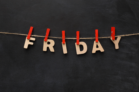Word Friday spelled with wooden letters on black background. Characters handing on red clothespins,...
