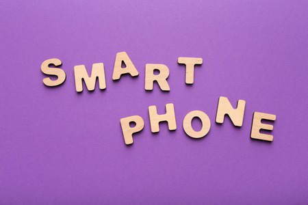 Smartphone word spelled with wooden letters on violet background, copy space, top view. Technology, communication and gadget conceptの写真素材