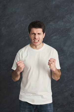 Portrait of angry man. Aggressive guy gesturing with fists, gray studio background. Psychotherapy exerciseの写真素材