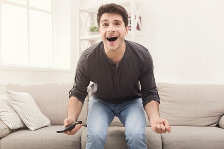 Excited man watching sports on tv and supporting favorite team, sitting on couch at home, copy spaceの写真素材