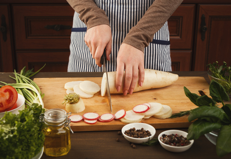 Woman cutting fresh turnip on wooden board. Natural eating, preparing healthy dietic vegetable salad at kitchen, side viewの写真素材