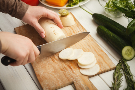 Woman cutting fresh turnip on wooden board. Natural eating, preparing healthy dietic vegetable salad at kitchen, top viewの写真素材
