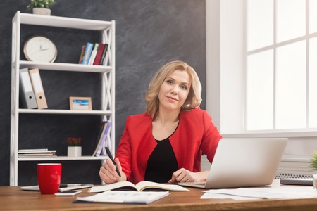 Happy businesswoman in formal wear sitting at wooden desk in modern office and working with documents, copy spaceの写真素材