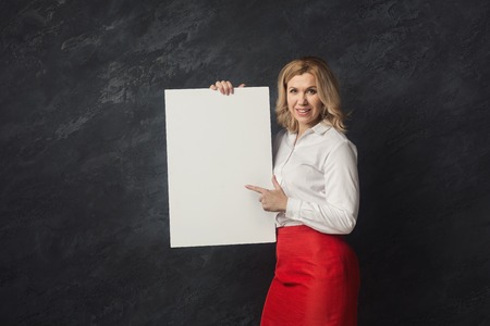 Happy businesswoman with blank white paper. Happy woman holding advertising sheet and pointing on it, copy spaceの写真素材